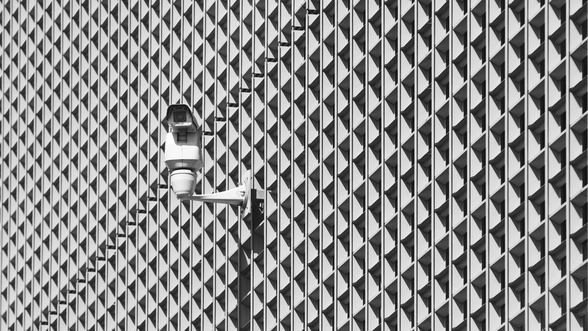 A security camera mounted on a building facade with a repeating metal pattern.