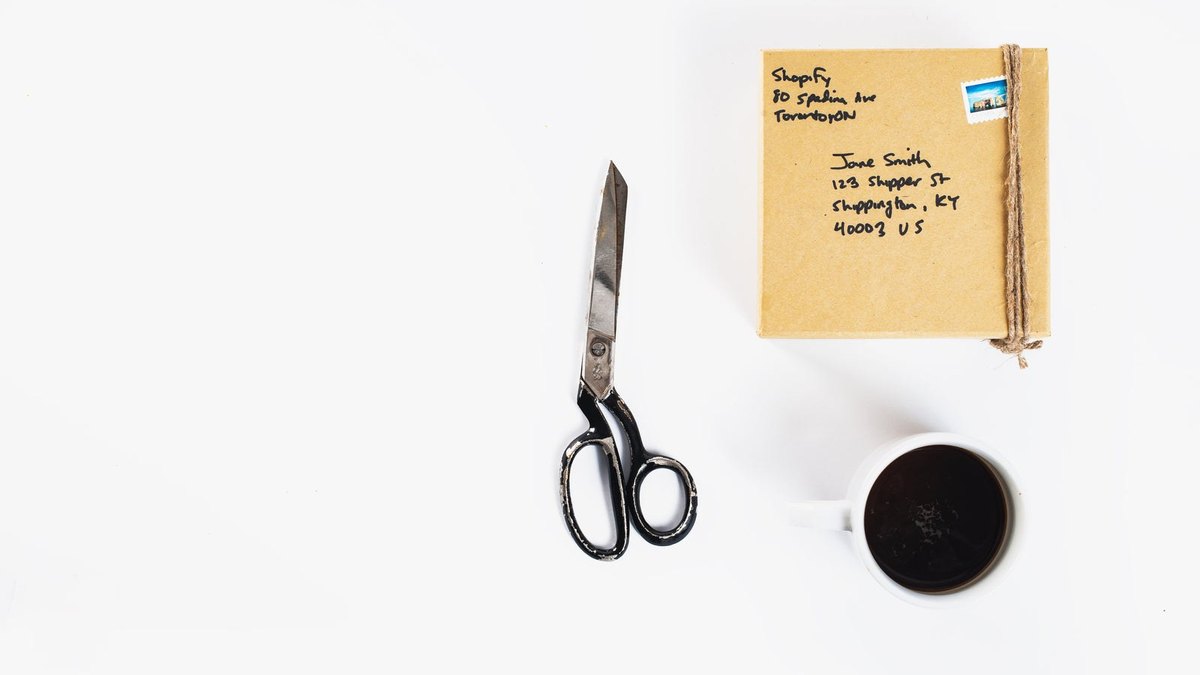 A padded envelope, scissors and a roll of tape arranged on a white surface.