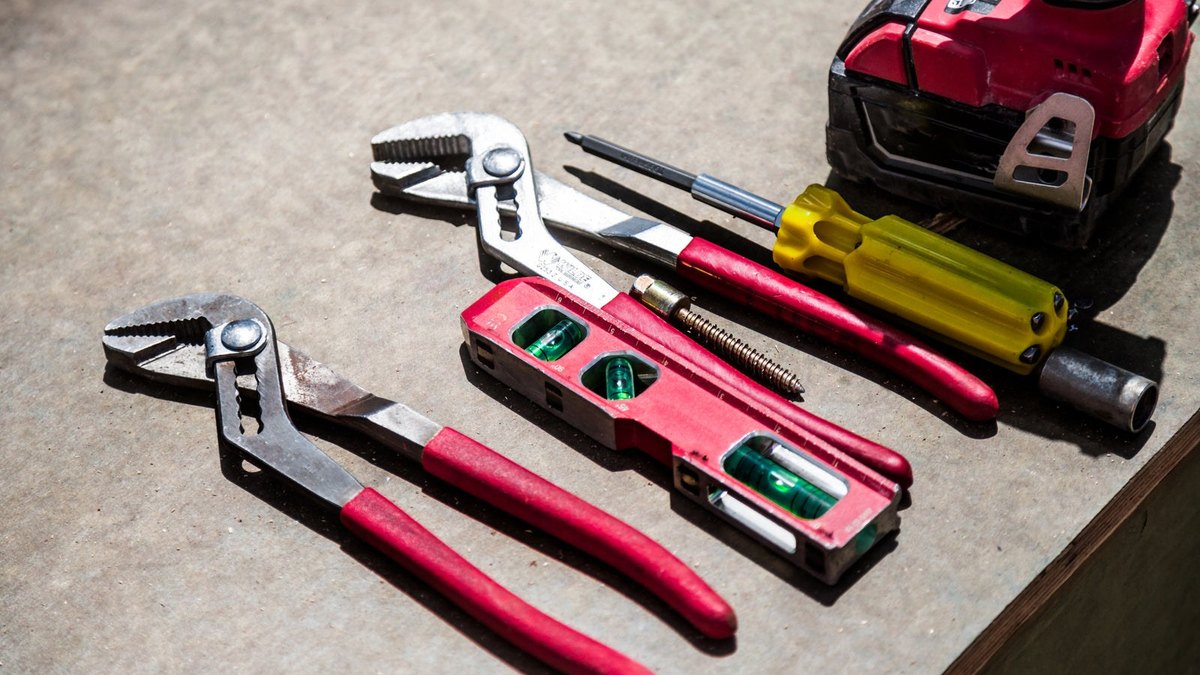 Pliers, screwdrivers, a spirit level and a tape measure laid out on a work surface.