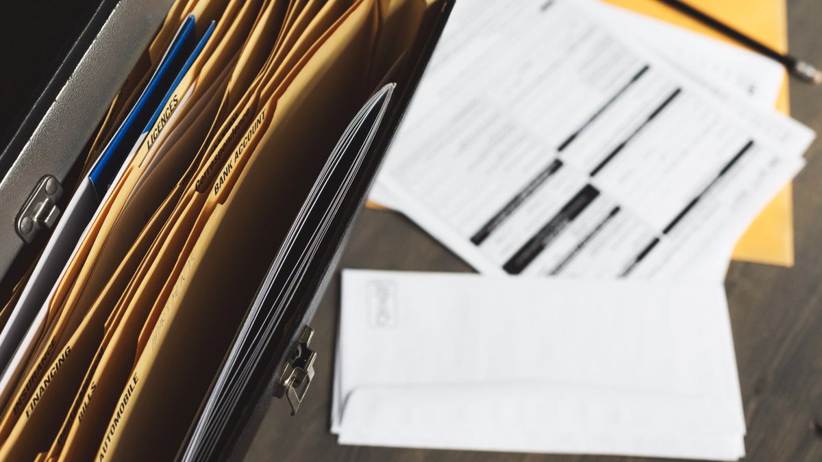 Paper folders in an open filing case beside loose documents.