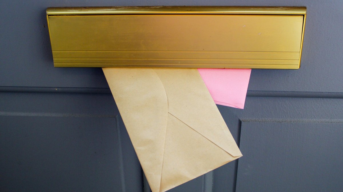 Envelopes protruding from a brass letter slot in a grey door.