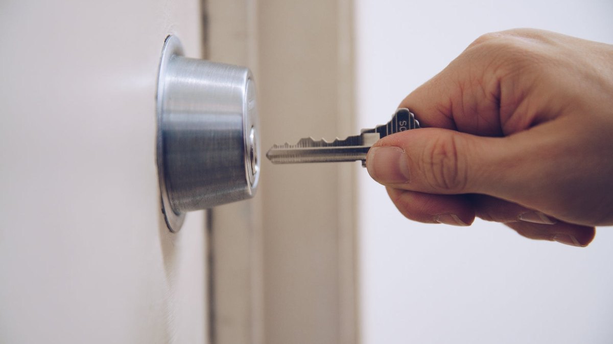 A hand holding a metal key in front of a door lock.