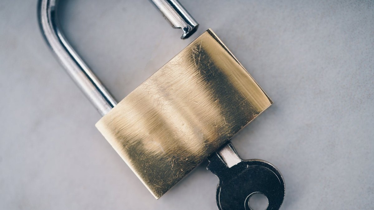 A brass padlock with its shackle open and a key in the lock.