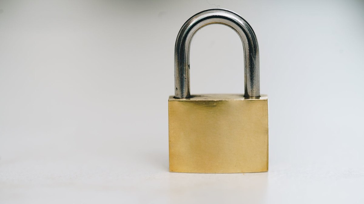 A closed brass padlock standing on a pale surface.
