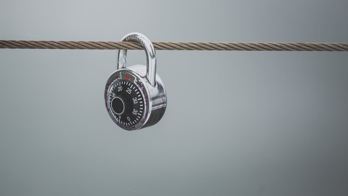 A combination padlock hanging from a taut metal cable.