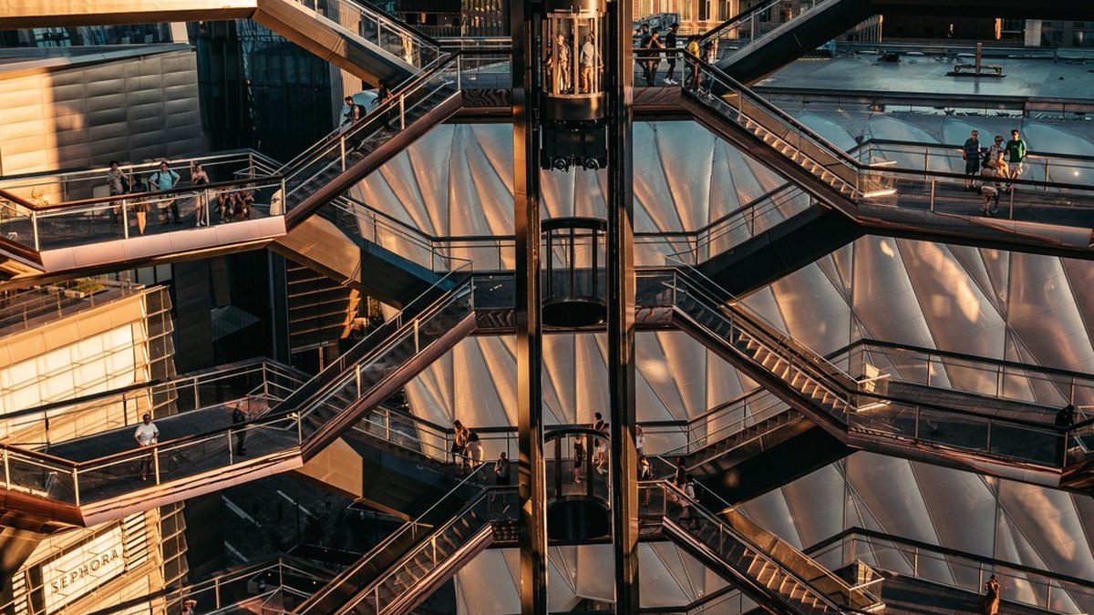 Several levels of stairs and walkways around a glass lift shaft.