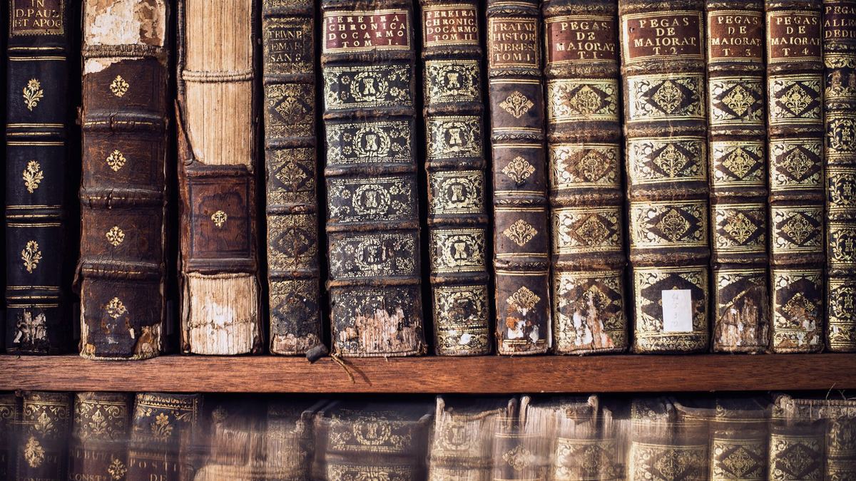 Worn leather-bound books arranged upright on a wooden library shelf.