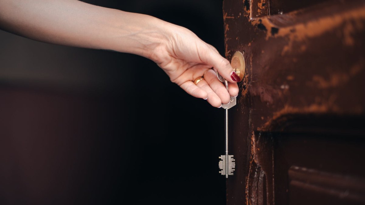 A hand holding a long metal key beside an old wooden door.