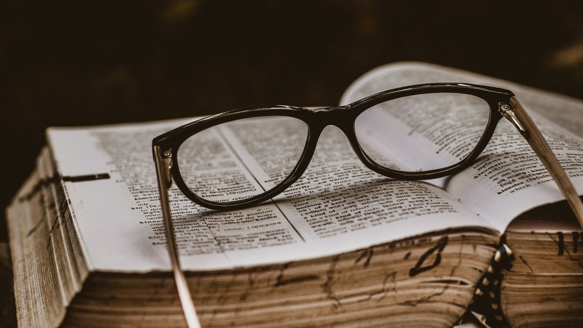 Dark-framed reading glasses resting on the pages of an old open book.