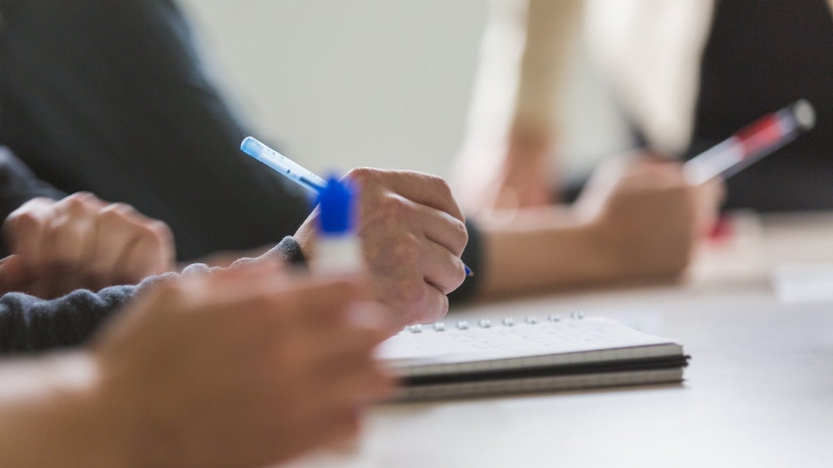 Hands taking notes with pens in notebooks during a meeting.