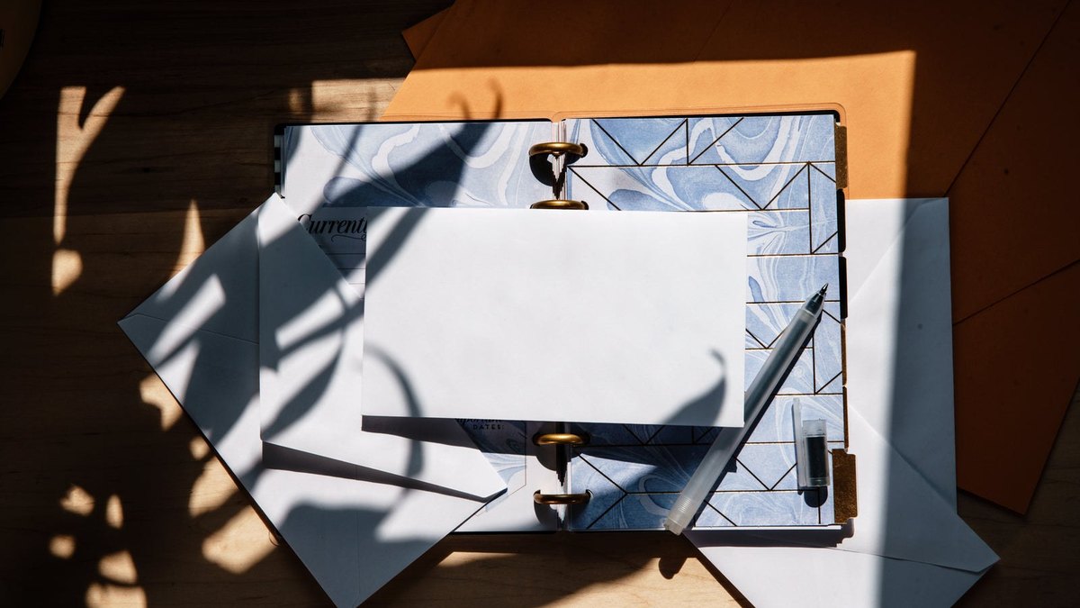 A blank white envelope lying on a notebook in angled sunlight.