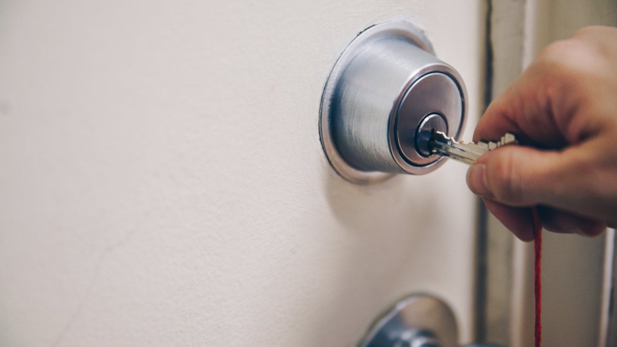 A hand turning a key in a silver deadbolt on a white door.