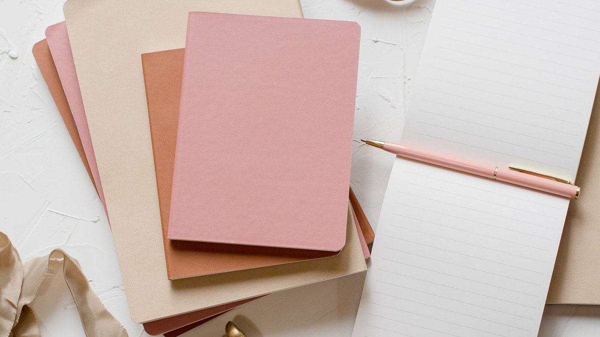 Pink and brown notebooks beside an open lined notebook and pink pencil.