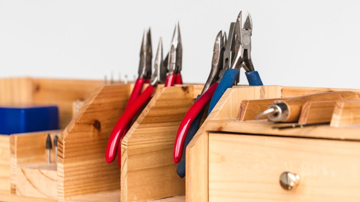 Pliers and cutters organised in compartments on a wooden workbench.