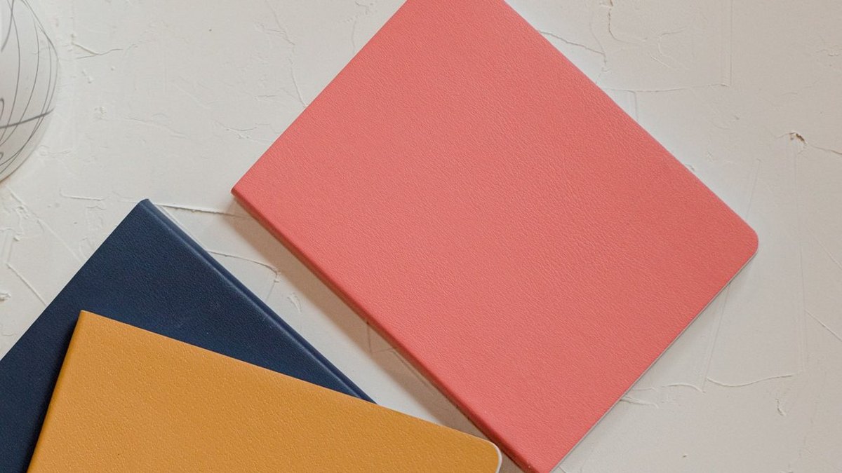 Pink, blue and yellow notebooks arranged on a pale desk.
