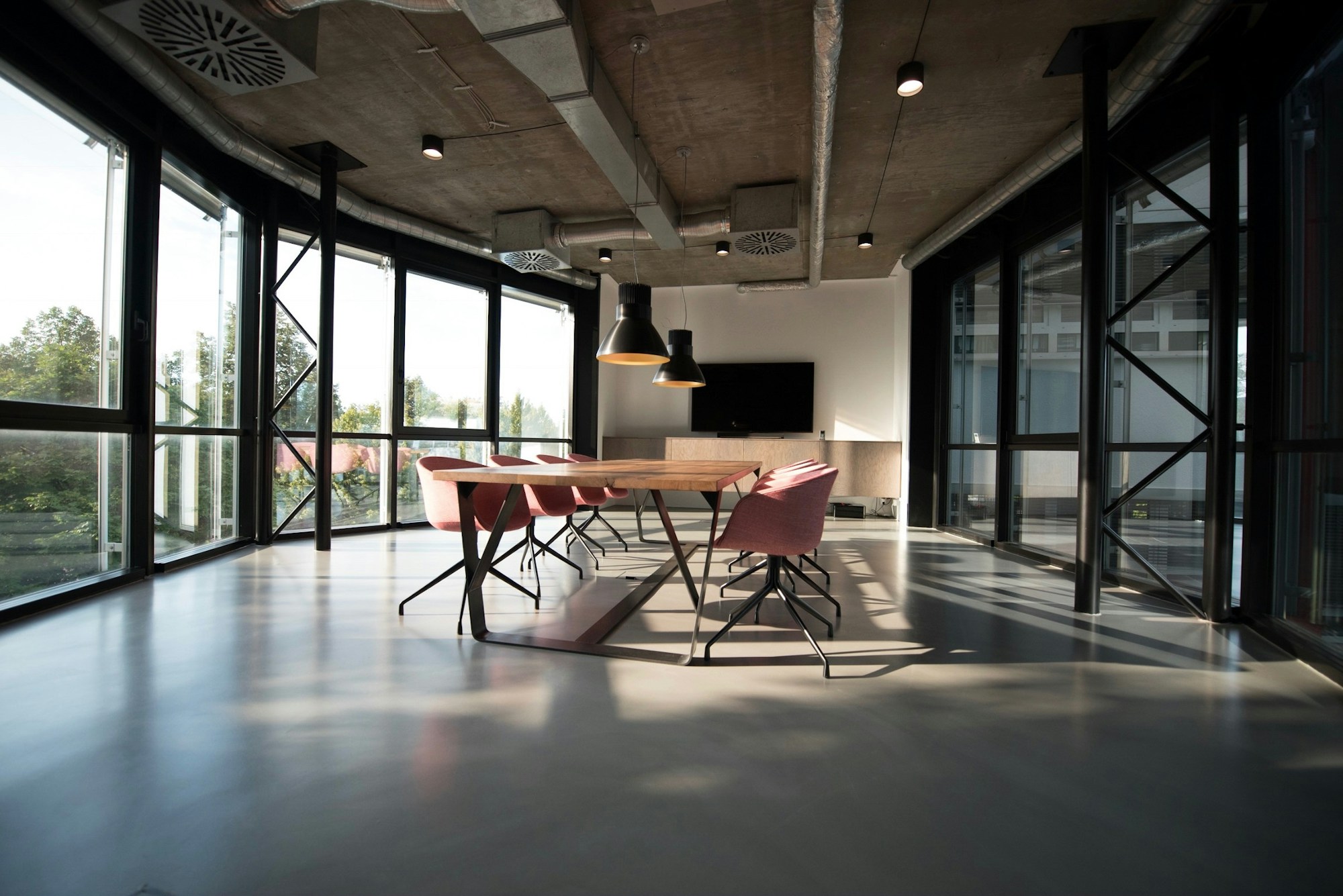 A bright shared workspace with a meeting table, chairs and tall windows.
